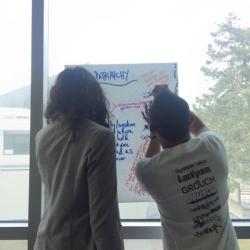 Two instructors writing on paper hung on window
