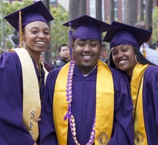 Three smiling Metro graduates in cap and gown